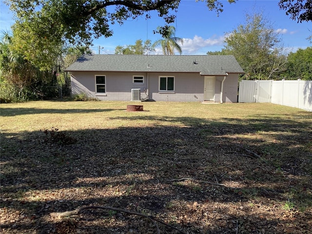 back of house featuring a shingled roof, fence, a lawn, concrete block siding, and a gate