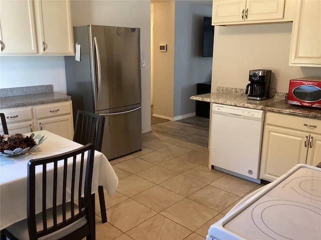 kitchen featuring stove, white dishwasher, stainless steel fridge, light tile patterned flooring, and white cabinetry