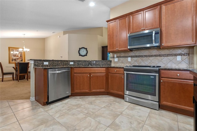 kitchen with sink, hanging light fixtures, dark stone countertops, a notable chandelier, and stainless steel appliances