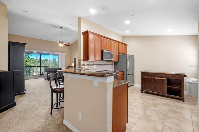 kitchen featuring ceiling fan, tasteful backsplash, vaulted ceiling, a breakfast bar area, and appliances with stainless steel finishes