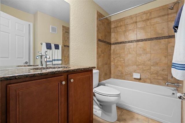 full bathroom featuring vanity, tile patterned floors, tiled shower / bath combo, toilet, and a textured ceiling