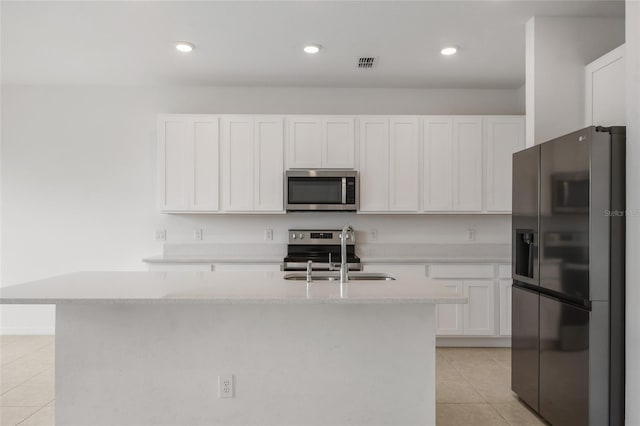 kitchen with sink, an island with sink, appliances with stainless steel finishes, light tile patterned flooring, and white cabinetry