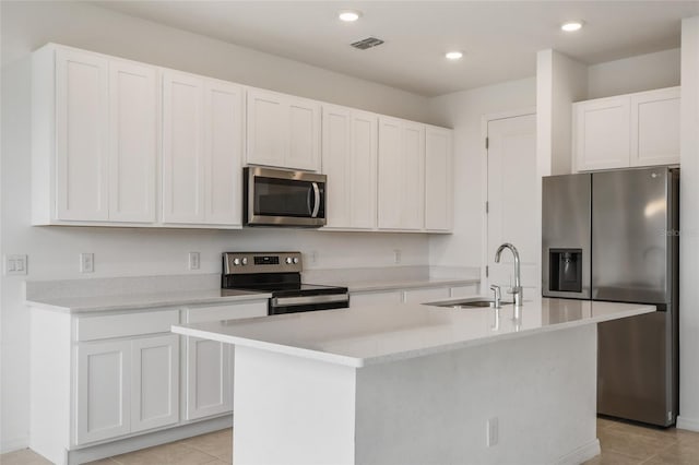 kitchen with light tile patterned flooring, a kitchen island with sink, white cabinets, and stainless steel appliances