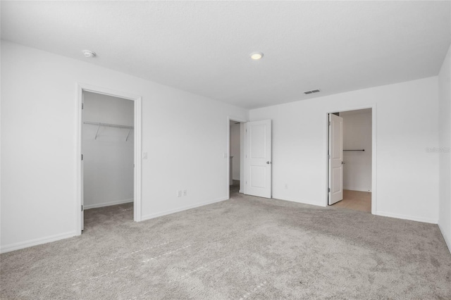 unfurnished bedroom featuring connected bathroom, a spacious closet, a closet, and light carpet