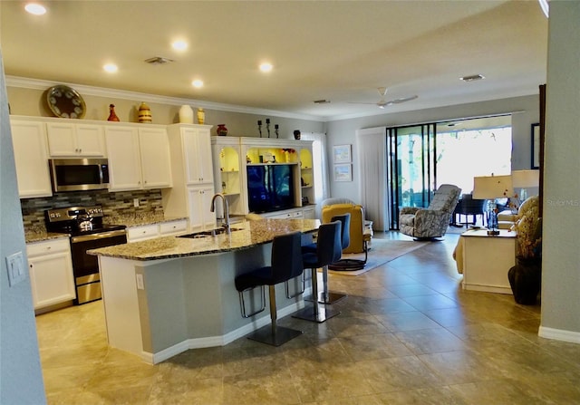 kitchen with white cabinets, an island with sink, appliances with stainless steel finishes, light stone counters, and a sink