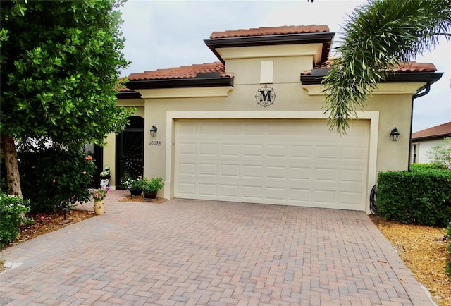 mediterranean / spanish home with decorative driveway, an attached garage, a tile roof, and stucco siding