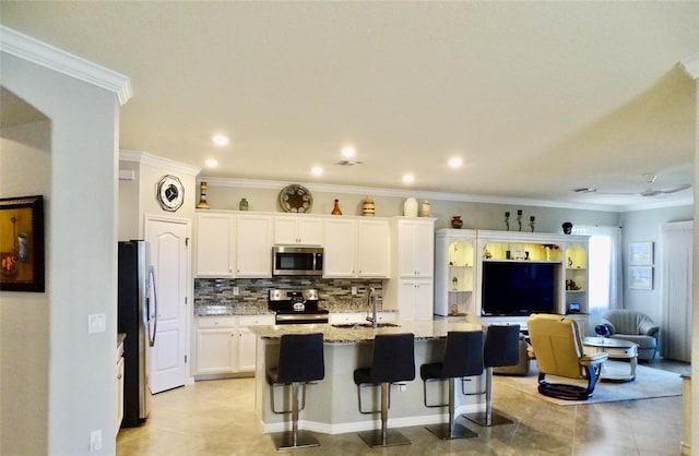 kitchen with white cabinetry, appliances with stainless steel finishes, light stone countertops, tasteful backsplash, and a center island with sink