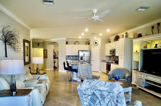 living room featuring a ceiling fan, arched walkways, visible vents, and crown molding