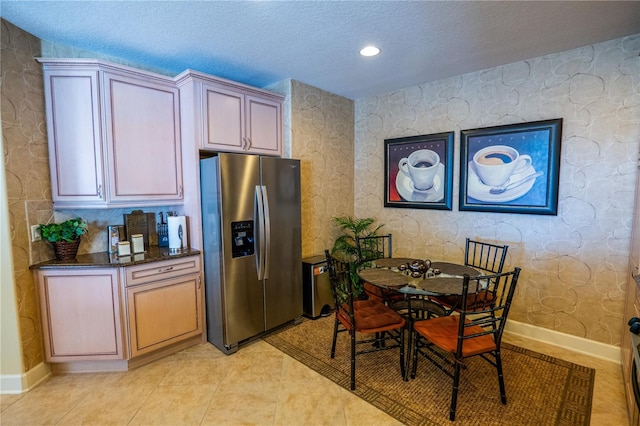 kitchen with stainless steel refrigerator with ice dispenser, dark stone counters, a textured ceiling, light brown cabinetry, and light tile patterned flooring