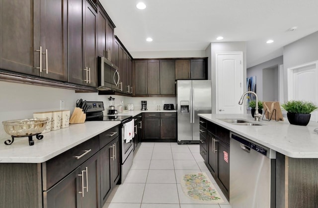 kitchen featuring appliances with stainless steel finishes, dark brown cabinets, sink, an island with sink, and light tile patterned flooring