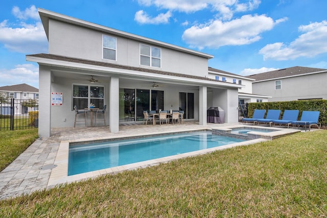 back of property with a yard, ceiling fan, a swimming pool with hot tub, and a patio