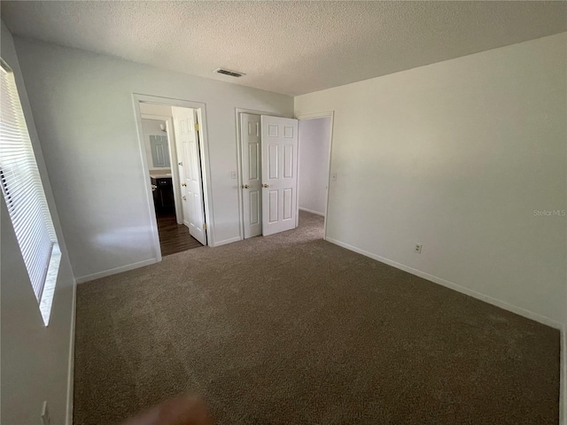 unfurnished bedroom with multiple windows, a textured ceiling, and dark colored carpet