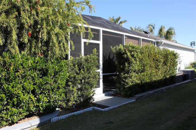 view of side of property featuring a sunroom, a yard, and central AC