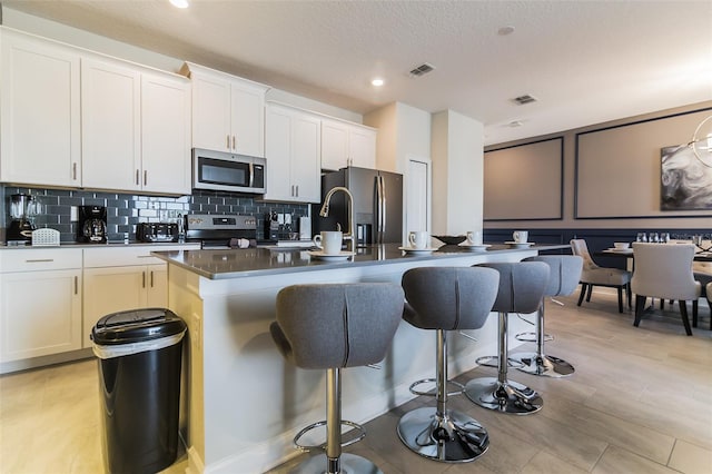 kitchen with a center island with sink, white cabinets, a kitchen bar, and appliances with stainless steel finishes