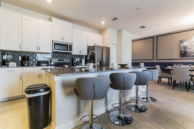 8943 Cabot Cliffs Dr, Davenport, FL 33896 - kitchen featuring stainless steel appliances, a breakfast bar, an island with sink, tasteful backsplash, and dark countertops