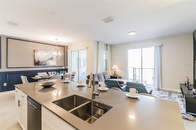 kitchen featuring stainless steel dishwasher, a sink, open floor plan, a chandelier, and white cabinetry