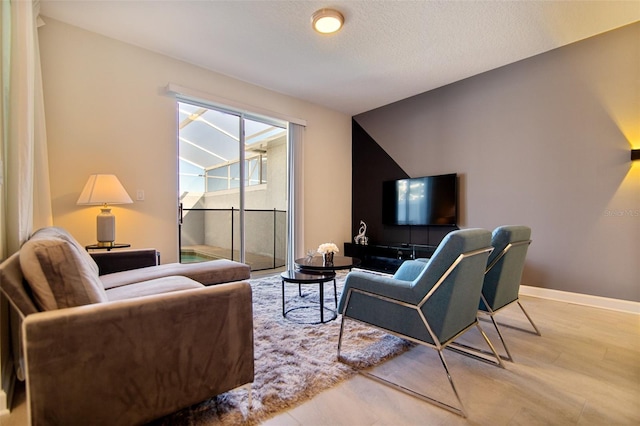 living area with baseboards, light wood-type flooring, and a textured ceiling