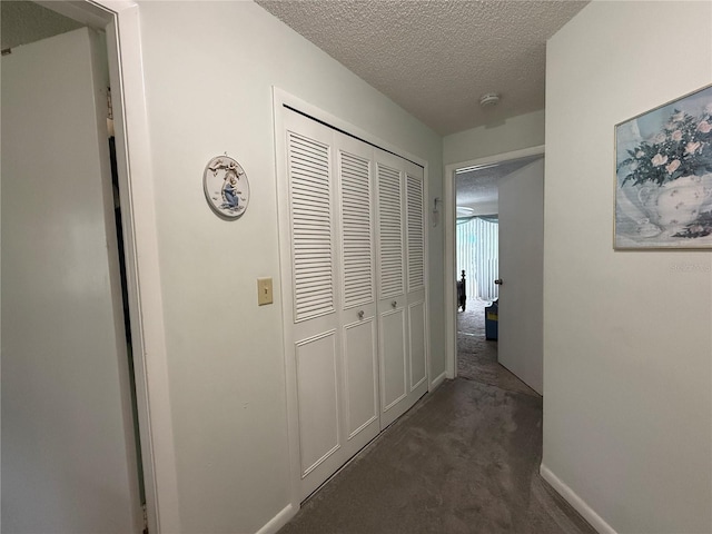 corridor with dark carpet and a textured ceiling