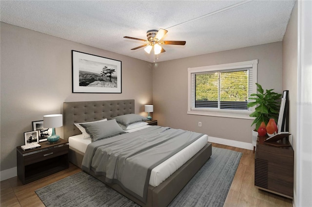 bedroom featuring ceiling fan, a textured ceiling, baseboards, and wood finished floors