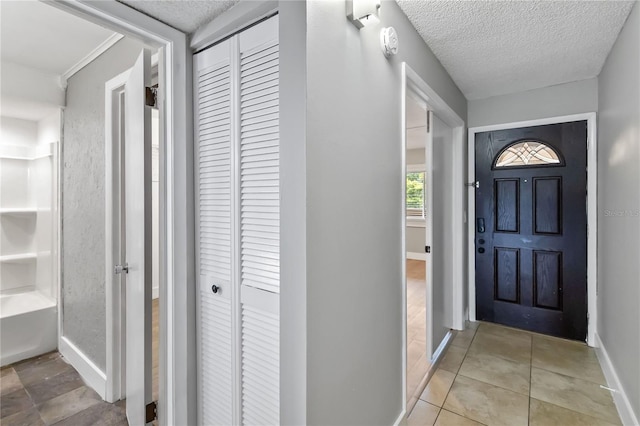 entrance foyer with a textured ceiling, baseboards, and light tile patterned floors