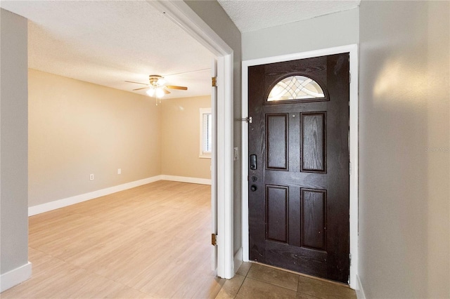 foyer with a textured ceiling, ceiling fan, light wood-type flooring, and baseboards