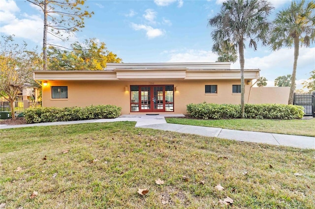 exterior space with french doors, stucco siding, a lawn, and fence