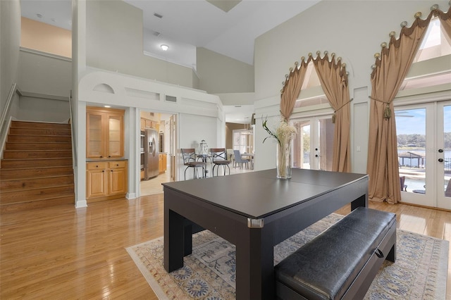 recreation room featuring light wood-type flooring, a towering ceiling, and french doors