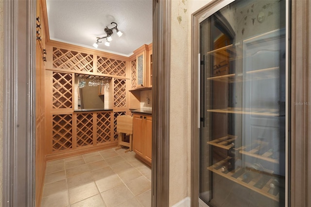 wine cellar with ornamental molding, a textured ceiling, wine cooler, and track lighting