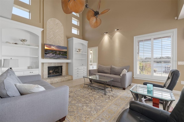 tiled living room with a brick fireplace, a towering ceiling, built in features, and ceiling fan