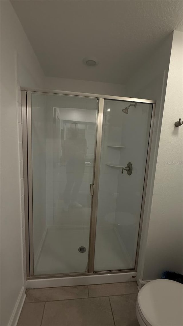 bathroom with toilet, walk in shower, and tile patterned flooring