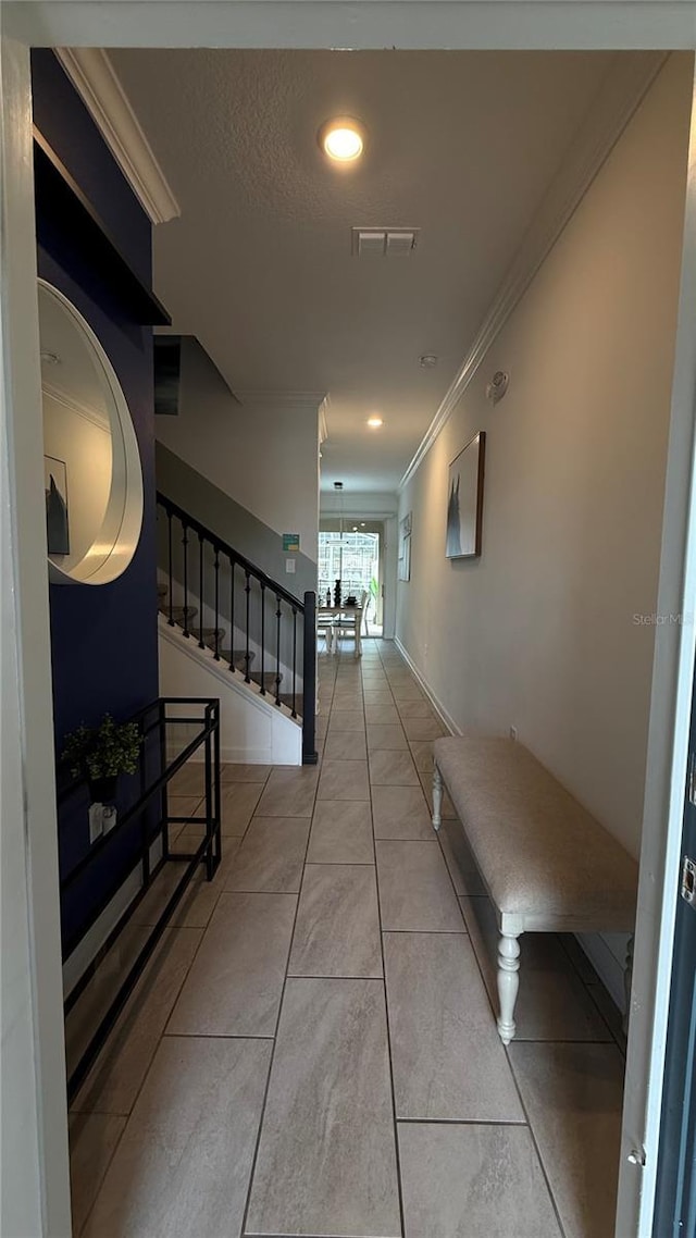 corridor featuring a textured ceiling, light tile patterned floors, and ornamental molding