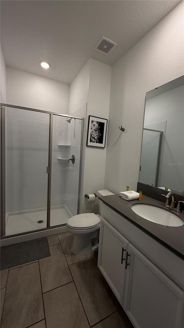 bathroom with toilet, vanity, an enclosed shower, and tile patterned flooring