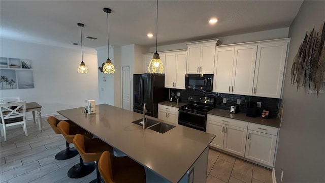 kitchen featuring pendant lighting, black appliances, a kitchen bar, sink, and a kitchen island with sink