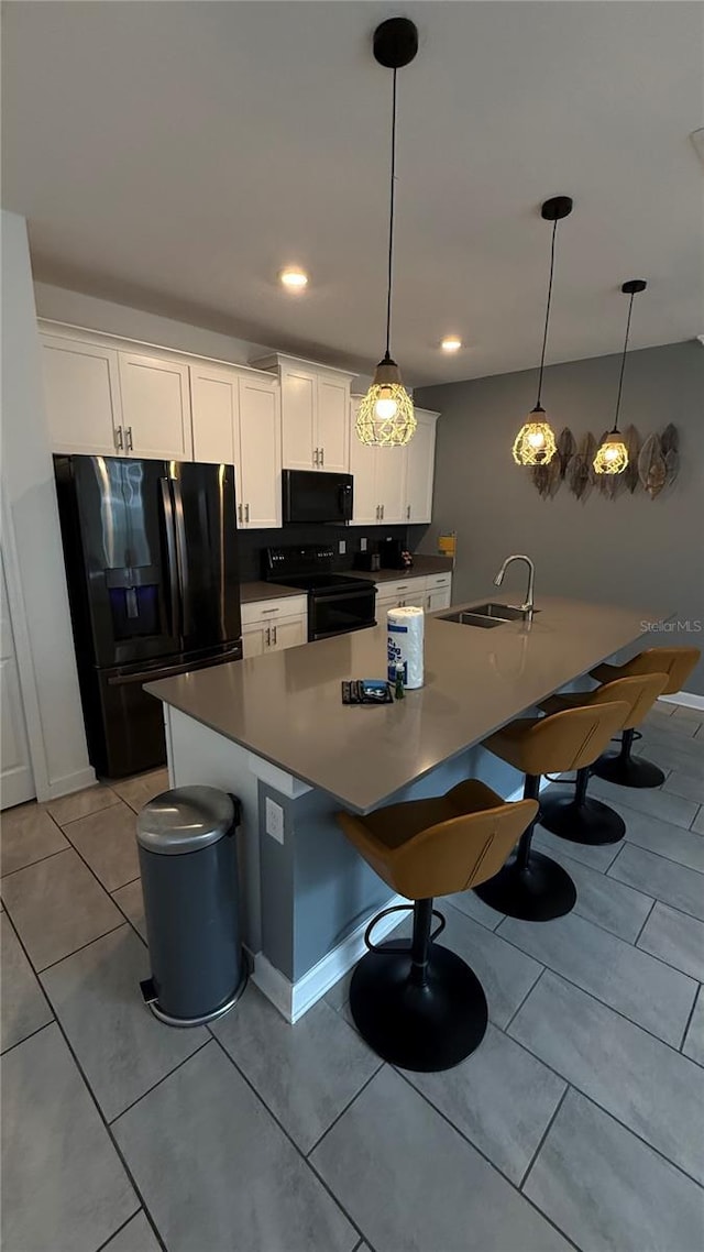 kitchen featuring white cabinets, black appliances, a center island, decorative light fixtures, and sink