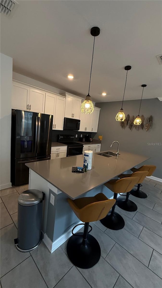 kitchen with white cabinets, black appliances, a center island, decorative light fixtures, and sink