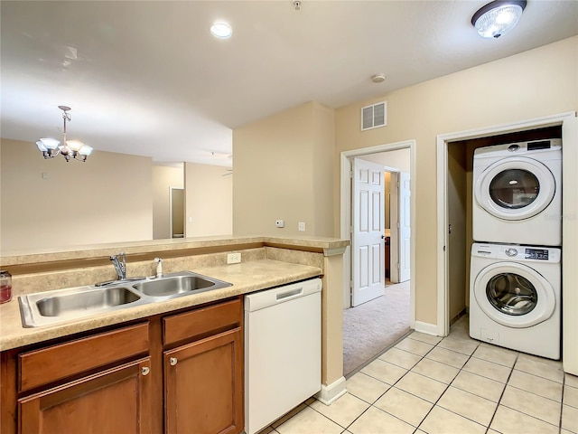 kitchen featuring an inviting chandelier, white dishwasher, sink, hanging light fixtures, and stacked washer / dryer