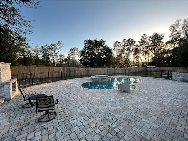 pool at dusk with an in ground hot tub and a patio