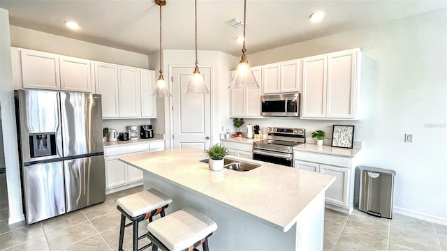 kitchen with white cabinets, hanging light fixtures, light stone countertops, an island with sink, and appliances with stainless steel finishes