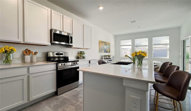 kitchen with white cabinets, stainless steel appliances, a center island with sink, and sink