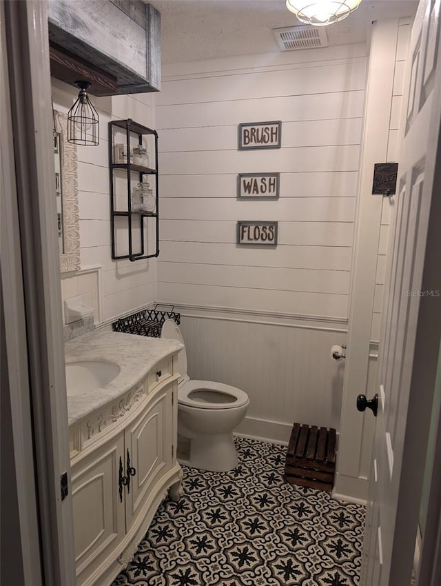 bathroom featuring a textured ceiling, wood walls, toilet, and vanity