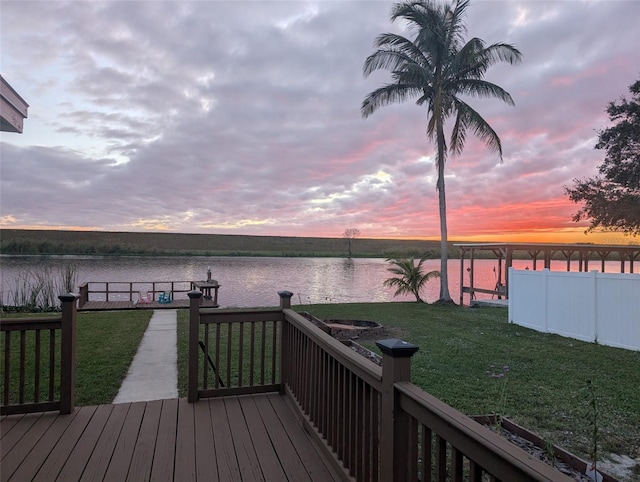 deck at dusk featuring a water view and a yard