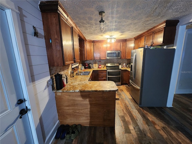 kitchen featuring appliances with stainless steel finishes, dark wood-type flooring, sink, hanging light fixtures, and kitchen peninsula