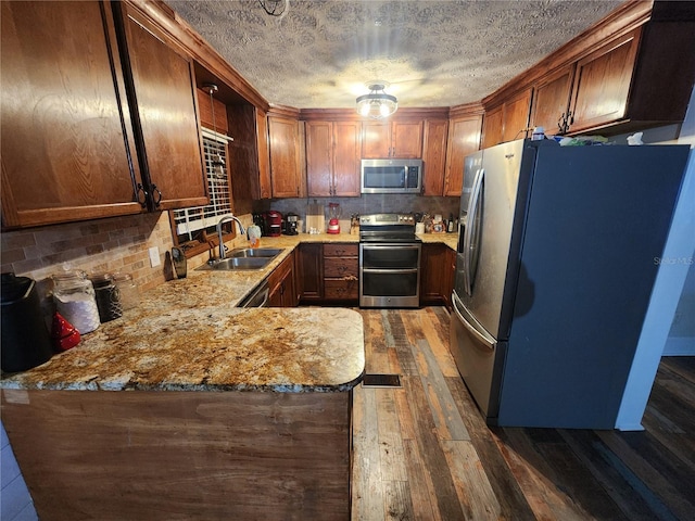 kitchen with kitchen peninsula, sink, dark wood-type flooring, light stone counters, and stainless steel appliances