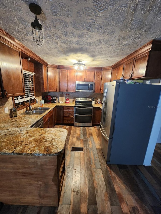 kitchen with light stone countertops, appliances with stainless steel finishes, sink, kitchen peninsula, and dark wood-type flooring