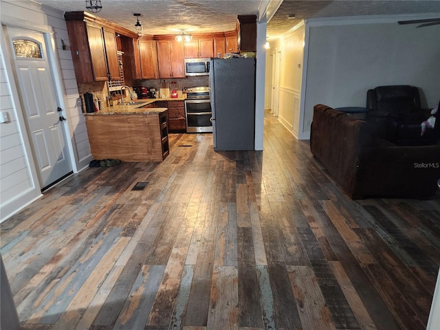 kitchen with crown molding, sink, kitchen peninsula, dark wood-type flooring, and stainless steel appliances