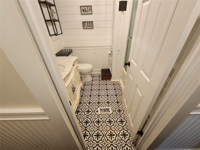 bathroom with vanity, toilet, and wooden walls