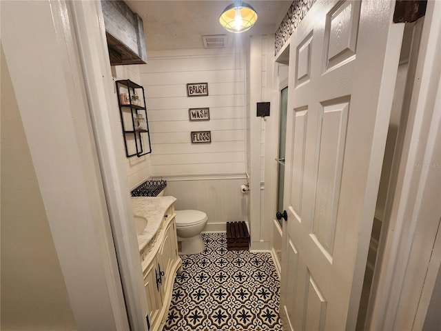 bathroom with toilet, vanity, and wooden walls