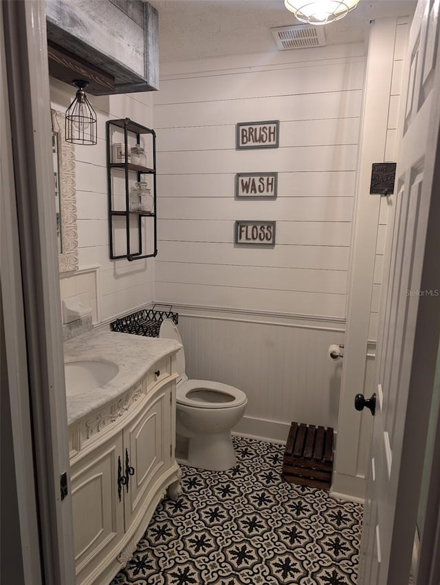 bathroom featuring tile patterned flooring, a textured ceiling, toilet, vanity, and wood walls