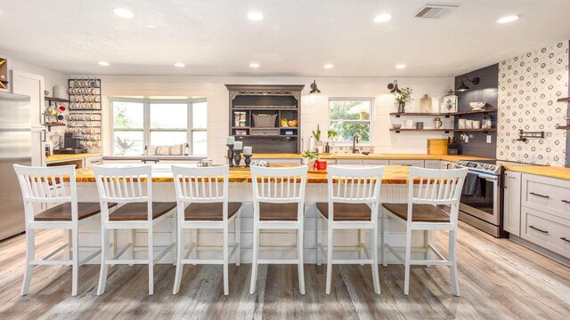 kitchen with a wealth of natural light, a breakfast bar, wooden counters, and appliances with stainless steel finishes