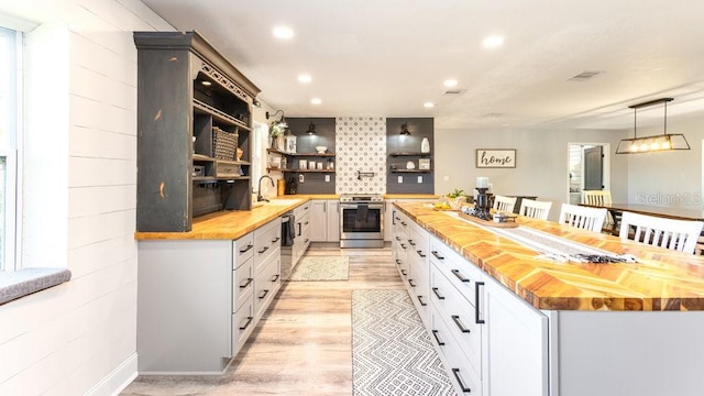 kitchen featuring butcher block counters, white cabinetry, stainless steel appliances, decorative light fixtures, and light wood-type flooring